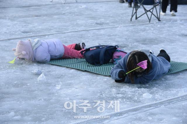 2023년 1월 열린 화천산천어축제장의 얼음낚시터에서 두 어린이가 엎드린 자세로 낚시를 하고 있다사진박종속 기자