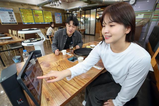 모델이 서울 종로구의 한 음식점에서 KT 으랏차차 패키지에 포함된 하이오더와 AI 서빙로봇을 소개하는 모습사진KT