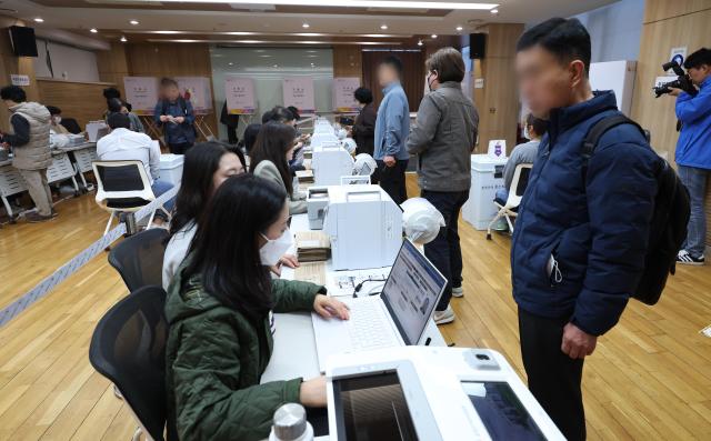 Election officials check voters identities before they vote at a community center in Seoul April 5 Yonhap