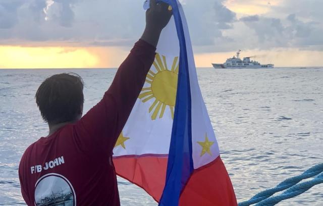 지난 5월 16일현지시간 남중국해에서 스카버러 암초중국명 황옌다오·黃岩島로 향하던 필리핀 어선을 중국 해경선이 막아서자 어민이 필리핀 국기를 들어 보이고 있다 EPA연합뉴스