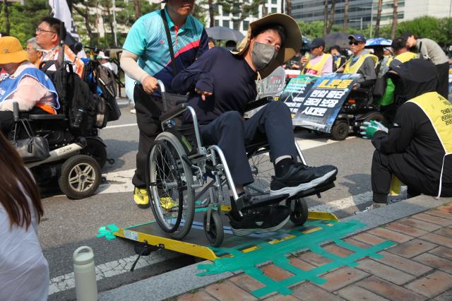 A protester in a wheelchair ascends a temporary ramp with assistance during the Move Toward Parade organized by SADD in front of the National Assembly on July 1 2024 AJU PRESS Han Jun-gu