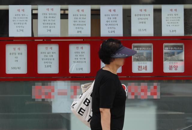 A pedestrian walks past real estate listings displayed in a window Yonhap Photo