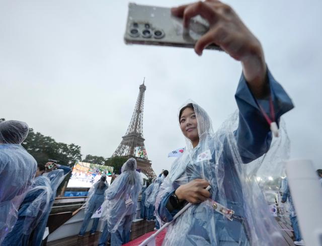 Asom Kim a physiotherapist from team South Korea takes a selfie with the Eiffel Tower from a boat down the Seine River in Paris France during the opening ceremony of the 2024 Summer Olympics Friday July 26 2024 APYonhap