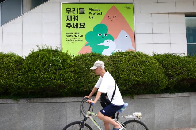 A person rides a bicycle past the Please protect us exhibition sign in front of Cheonggyecheon Museum Seoul on July 30 2024 AJU PRESS Han Jun-gu