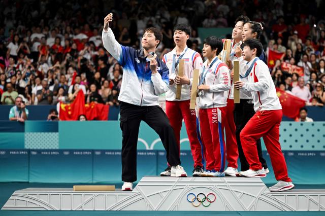 Bronze medalists South Koreas Lim Jonghoon L takes a selfie picture with his mobile as he celebrates on the podium with  gold medalists Chinas Wang Chuqin rear R and Chinas Sun Yingsha front L silver medalists North Koreas Ri Jong Sik 2nd L and North Koreas Kim Kum Yong C and bronze medallist and teammate South Koreas Shin Yubin rear R at the end of their mixed table tennis doubles competition at the Paris 2024 Olympic Games at the South Paris Arena in Paris on July 30 2024 AFP-Yonhap