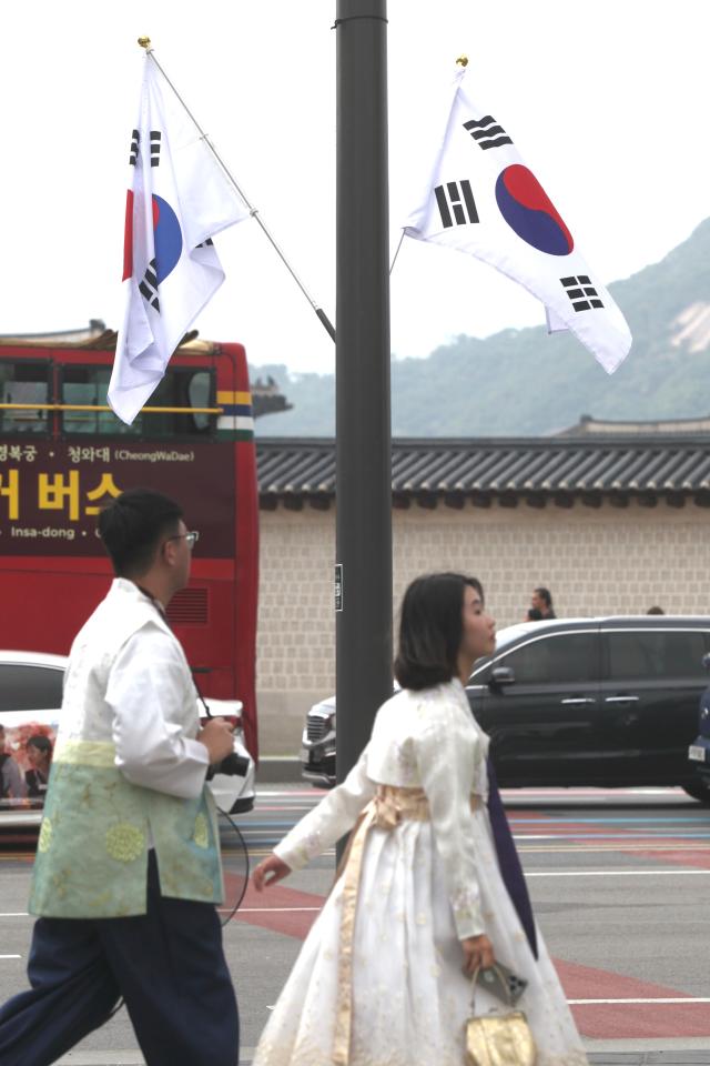 Visitors wearing hanbok traditional Korean attire walk past a display of The national flag of Korean near Gyeongbok Palace on Aug 14 2024