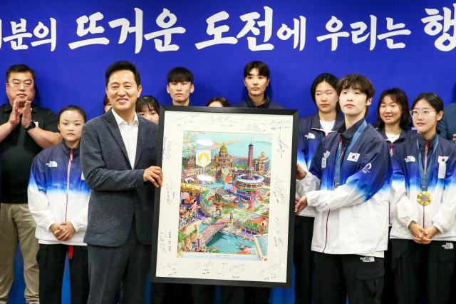 Taekwondo athlete Lee Da-bin right presents a commemorative poster of the Paris Olympics to Seoul Mayor Oh Se-hoon left at Seoul City Hall on Aug 19 2024 AJU PRESS Kim Dong-woo