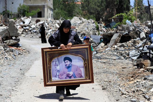 A woman carries a portrait of Hezbollah leader Sayyid Hassan Nasrallah as she passes by houses destroyed by Israeli airstrikes in South Lebanon June 29 2024 AP-Yonhap 