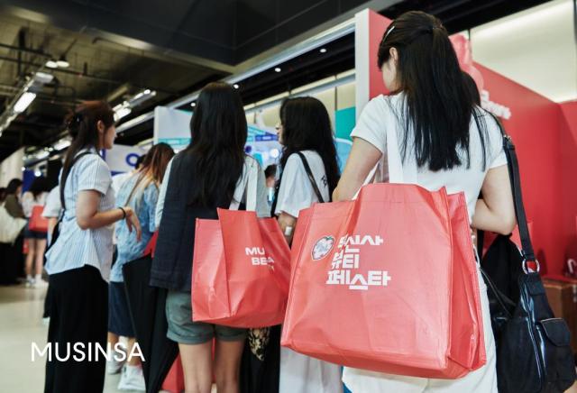 무신사 뷰티 페스타에서 코랄색 구디백을 착용한 이삼십대 여성 고객들이 줄을 서서 기다리고 있다 사진무신사