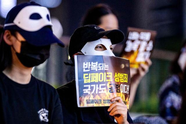 Activists wearing eye masks hold posters reading Repeated deepfake sex crimes the state is an accomplice too during a protest against deepfake porn in Seoul on Aug 30 2024 AFP-Yonhap