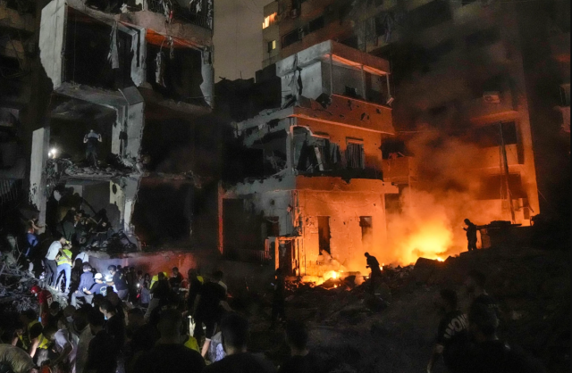 People stand in front of destroyed buildings on fire after an Israeli airstrike in Beirut Lebanon on Oct 10 2024 AP-Yonhap