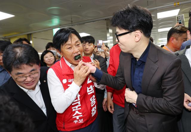 한동훈 국민의힘 대표가 27일 오전 인천 강화군 강화읍 강화풍물시장을 찾아 상인들과 인사하며 10·16 강화군수 보궐 선거 박용철 후보 지지를 호소하며 상인이 건넨 떡을 박 후보에게 먹여 주고 있다 사진연합뉴스