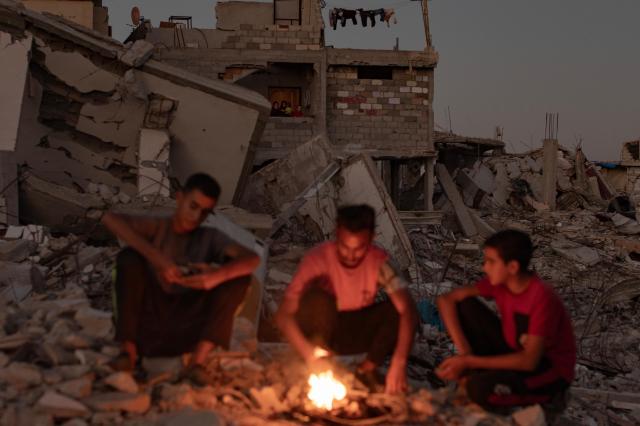 Palestinians sit by a fire amid the rubble of their demolished home in  southern Gaza Strip Palestine on Oct 20 2024