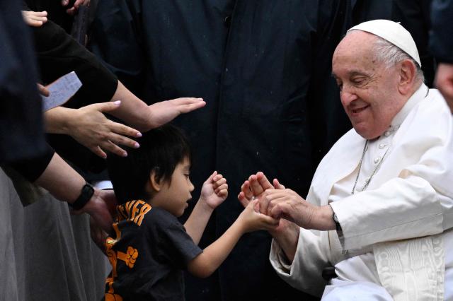 Pope Francis right gives candies to a child as he greets people at St Peters square in the Vatican Oct 23 2024 AFP-Yonhap