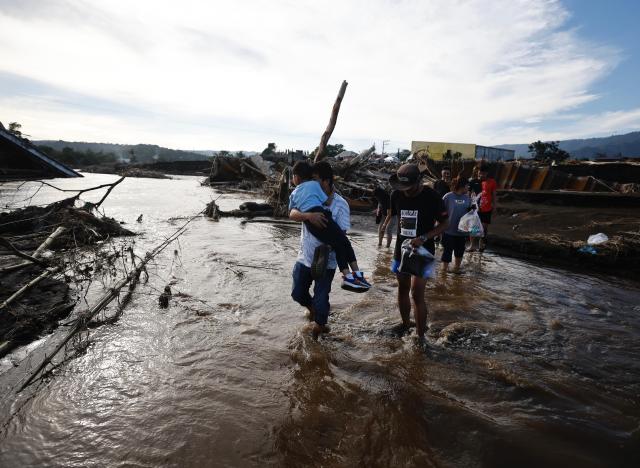 Villagers cross a river next to a damaged bridge in the aftermath of Tropical Storm Trami in the town of Laurel Batangas province Philippines Oct 27 2024 EPA-Yonhap