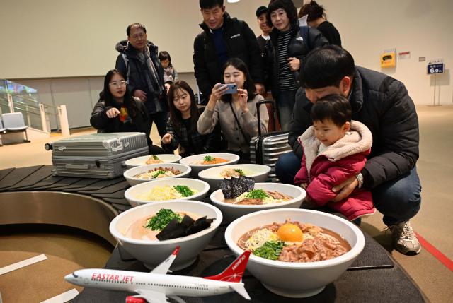 26일 오후 일본 도쿠시마공항에서 열린 이스타항공 도쿠시마 첫 취항 기념 행사에서 탑승객들이 공항 수하물 컨베이어 벨트에 전시된 도쿠시마 특산물 대형 라멘 모형을 관람하고 있다 사진이스타항공 