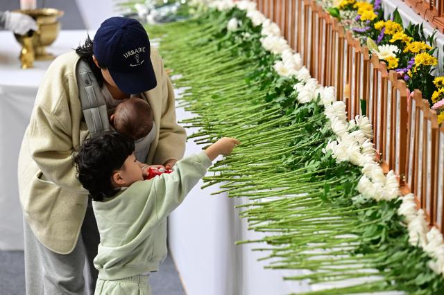 A child lays a flower at the joint memorial altar for victims of the Jeju Air crash set up at Muan Sports Park in South Jeolla Province Dec 30 2024 Joint Press Corps