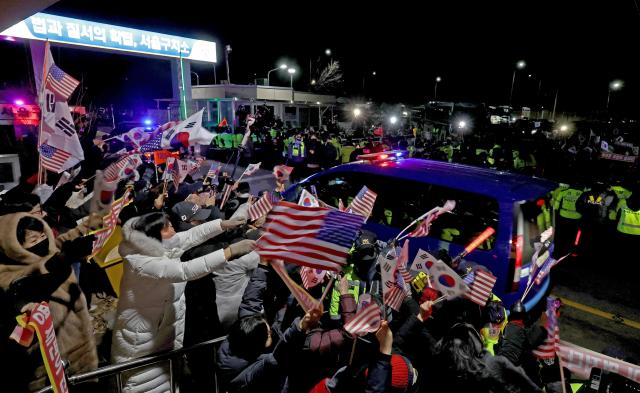 Supporters of President Yoon Suk Yeol wave flags as a vehicle carrying him returns to the Seoul Detention Center in Uiwang south of Seoul on Jan 18 2025 following a pretrial detention hearing Yonhap