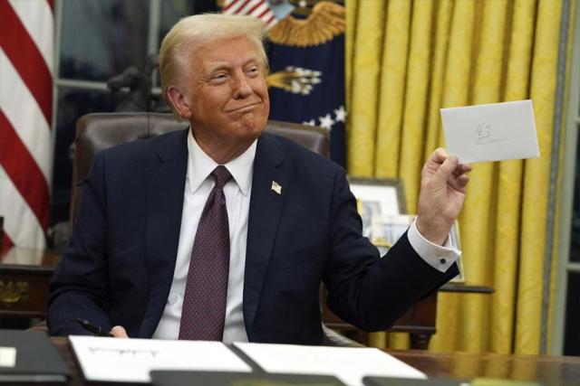 President Donald Trump holds up the letter that former President Joe Biden left for him in the desk as he signs executive orders in the Oval Office of the White House in Washington on Jan 20 2025 AP-Yonhap