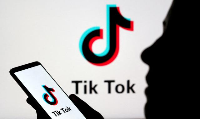 A person holding a smartphone with TikToks logo on the screen the logo also in the background as well Reuters-Yonhap