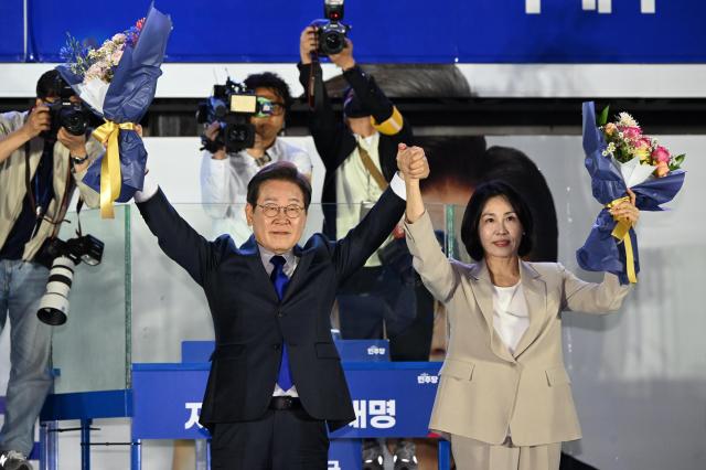 Democratic Party presidential candidate Lee Jae-myung who is projected to win South Korea’s 21st presidential election and his wife Kim Hye-kyung greet citizens with raised arms after receiving a bouquet at a public ballot broadcast event hosted by the party near the National Assembly in Yeouido Seoul on June 4 Joint Press Corps