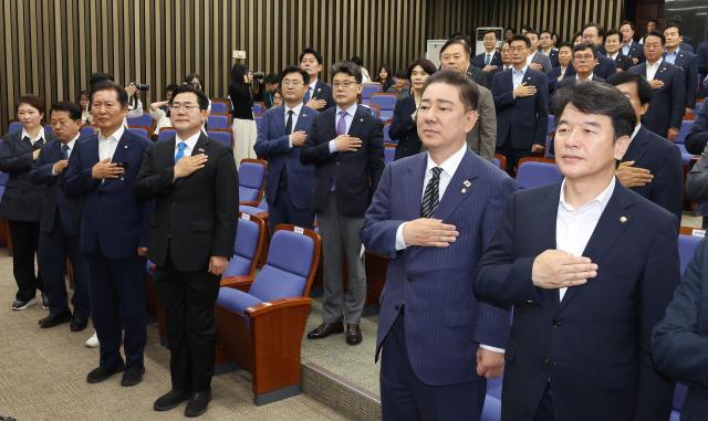 더불어민주당 김병기 당 대표 직무대행 겸 원내대표를 비롯한 당 대표 후보인 정청래·박찬대 의원 등 참석한 의원들이 24일 서울 여의도 국회에서 열린 의원총회에서 국기에 경례하고 있다 2
