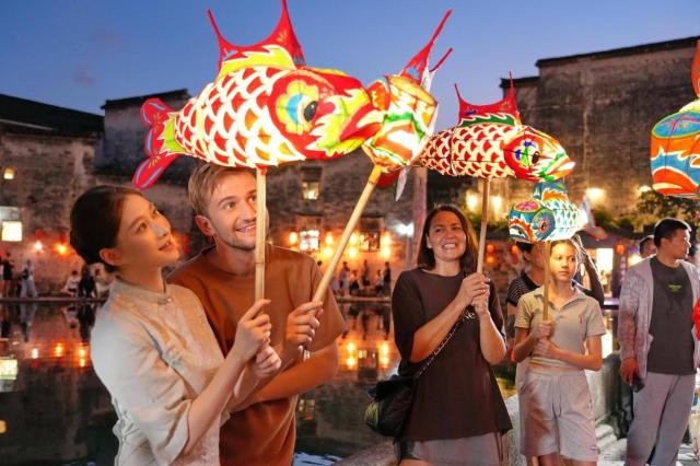 This photo taken on July 5 2025 shows foreign tourists experiencing fish-shaped-lantern parade in Hongcun village Yixian county Huangshan east Chinas Anhui province Peoples Daily
