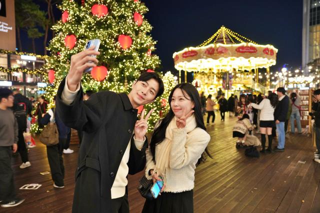 롯데타운 잠실 '초대형 크리스마스 트리'와 '크리스마스 마켓'에서 '2층 회전목마'를 배경으로 사진을 찍는 모델들[사진=롯데백화점]