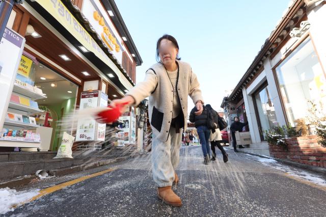 A shop owner spreads calcium chloride on an icy road in Bukchon Jongno District Seoul on December 5 2025 AJP Han Jun-gu