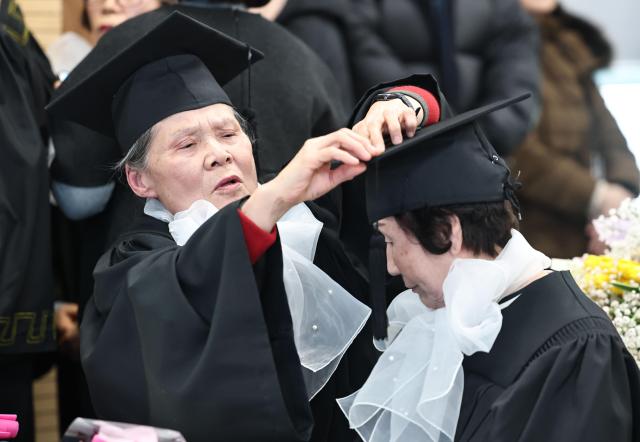 Adult graduates adjust each other’s mortarboards during the 2025 Neulpureum School elementary and middle school graduation ceremony at the annex building of Yeongdeungpo District Office in Seoul on Jan 28 2026 Yonhap