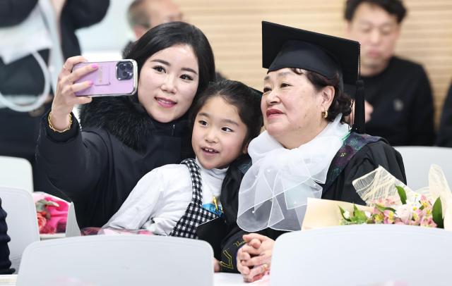 An adult graduate takes commemorative photos of family members during the 2025 Neulpureum School elementary and middle school graduation ceremony at the annex building of Yeongdeungpo District Office in Seoul on Jan 28 Yonhap