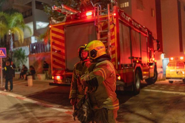 6일 이스라엘 텔아비브 외곽의 한 도시에서 발사체에 맞아 파손된 건물 밖에서 소방대원들이 진화 작업을 하고 있다 사진AFP

