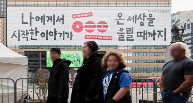 Tourists pass by a promotional banner for BTS near Gwanghwamun Square in central Seoul March 16 2026 AJP Yoo Na-hyun 20260316