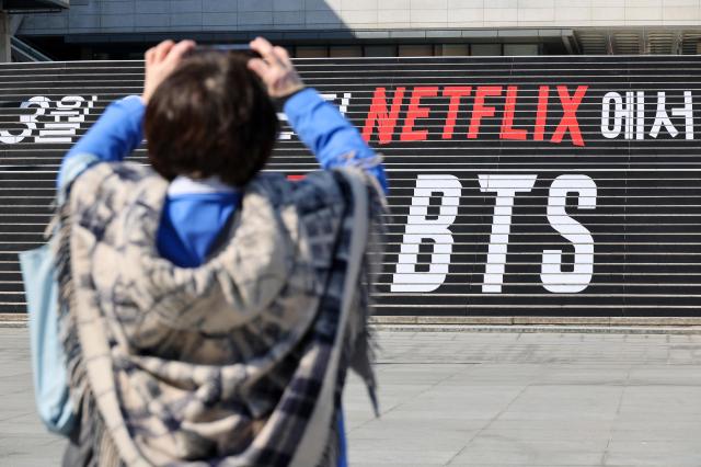 A tourist poses for a photo in front of a promotional banner for BTS’s comeback concert at the steps of Sejong Center for the Performing Arts in central Seoul on March 13 2026 AJP Yoo Na-hyun 20260313