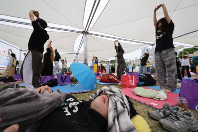 A participant sleeps at the 2026 Han River Napping Championship held at Mulbit Plaza in Yeouido Hangang Park while others partake in Yoga session before the competition Yeongdeungpo-gu Seoul May 2 2026 AJP Han Jun-gu