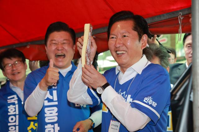 더불어민주당 정청래 총괄상임선거대책위원장이 22일 민주당 신용한 충북도지사 후보와 충북 충주자유시장을 방문해 상인과 인사하며 빵을 들어보이고 있다사진연합뉴스