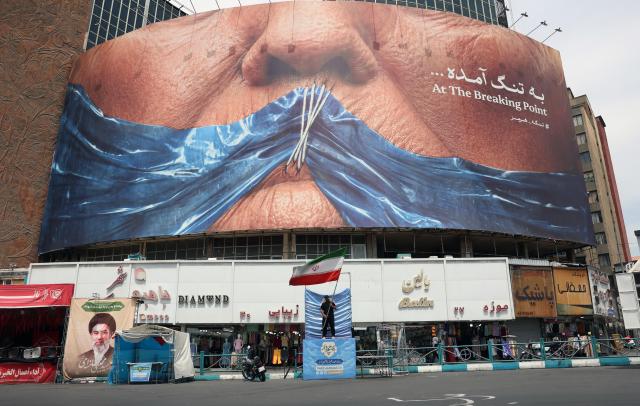 A man holds Irans national flag in front of a large anti-US billboard featuring US President Donald Trump and the Strait of Hormuz at Valiasr Square in Tehran Iran 28 May 2026 EPAYonhap