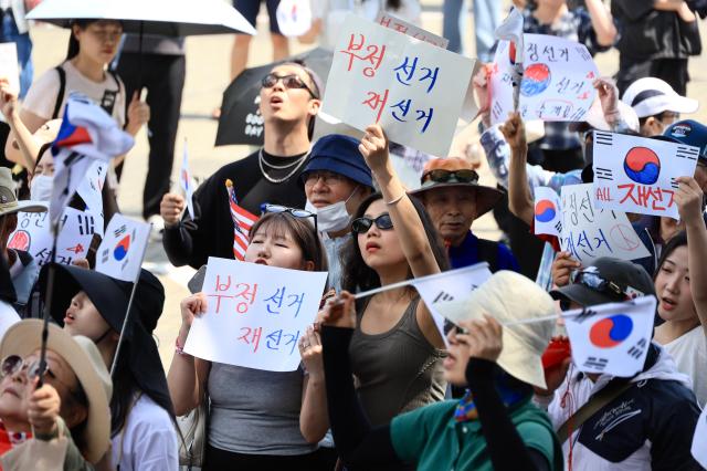 Protesters in 20s and 30s hold up handwritten posters demanding reelection on June 8 2026 AJP Han Jun-gu
