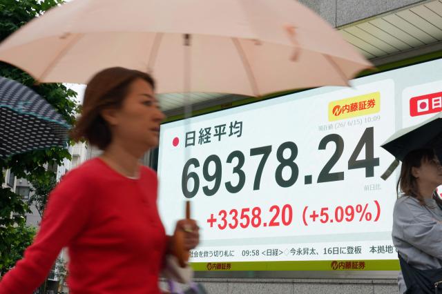 Pedestrians walk past an electronic quotation board displaying the Nikkei Stock Average on the Tokyo Stock Exchange in Tokyo on June 15 2026 AFPYonhap
