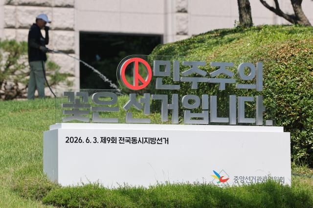 An official waters the lawn and flowers at the National Election Commission headquarters in Gwacheon Gyeonggi Province on June 15 2026 A sculpture bearing the phrase Elections are the flower of democracy is seen on the grounds as investigators intensify a probe into the ballot shortage controversy that marred the June 3 local elections Yonhap 