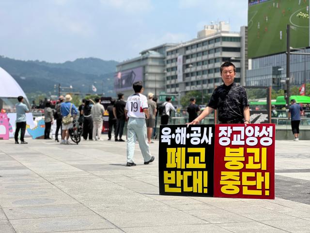 A man stages a protest in Gwanghwamun Seoul holding a sign opposing the proposed closure and integration of South Korea’s Army Navy and Air Force officer training academies on June 12 2026 AJP Kim Hee-su