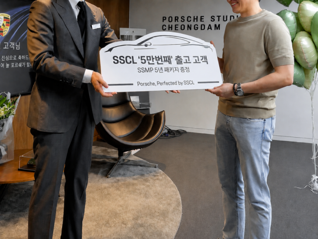 포르쉐 공식 딜러 SSCL 관계자가 5만 번째 출고 고객에게 기념 선물을 전달하고 있는 모습
