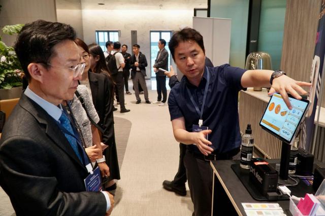 Min Byeong-seon, head of the KTO's Tourism Industry Division, visits the Prinker Korea booth and listens to CEO Yoon Tae-sik explain the use of the tattoo device.