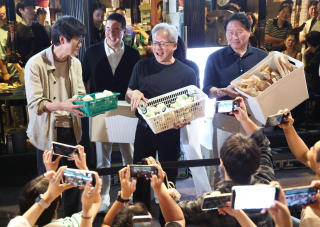 NVIDIA CEO Jensen Huang hands out banana-flavored milk and Sikhye a traditional Korean sweet rice drink to citizens outside the barbecue restaurant Hyungnim Jeoyo near Hongdae in Seoul on June 5 2026 ahead of a dinner meeting with SK Group Chairman Chey Tae-won LG Group Chairman Koo Kwang-mo and Naver Chairman Lee Hae-jin The gathering dubbed the samso meeting after samgyeopsal grilled pork belly and soju drew crowds of onlookers Yonhap
