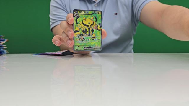 An AJP reporter ripping open a Pokémon card pack inside AJPs studio June 30 2026 AJP Han Jun-gu