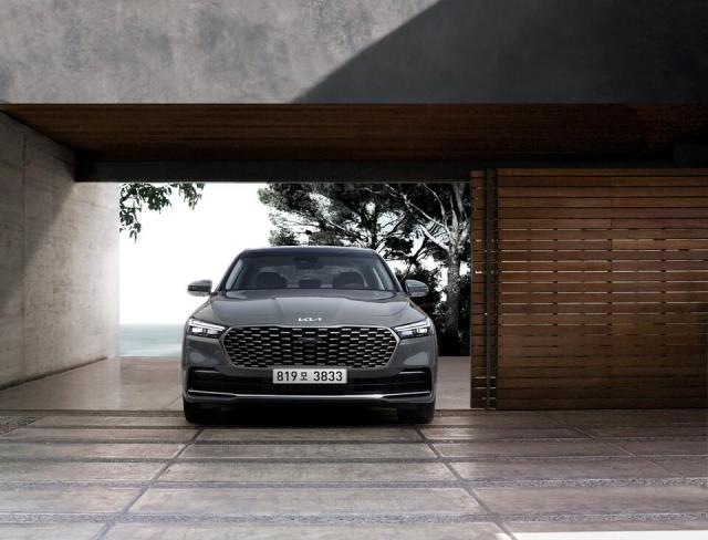 A Kia K9 is parked at the entrance of a modern coastal-style building in a promotional image for the sedan Kia is expected to end K9 production by the end of this year closing out the models 14-year run Courtesy of Hyundai Kia Motor Group