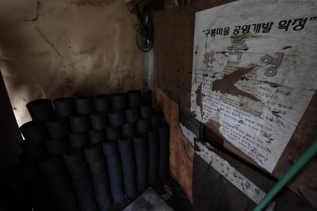 Stacked coal briquettes sit beside a tattered protest poster opposing redevelopment plans inside a home in Guryong Village Seoul South Korea AJP Han Jun-gu