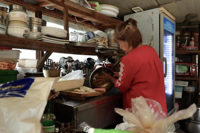 A woman in a red top prepares food at an outdoor kitchen counter in Guryong Village Seoul South Korea AJP Han Jun-gu