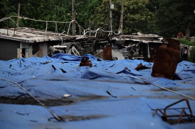  Blue tarps cover debris in the foreground as the charred remains of homes destroyed by fire stand in the background in Guryong Village Seoul South Korea AJP Han Jun-gu