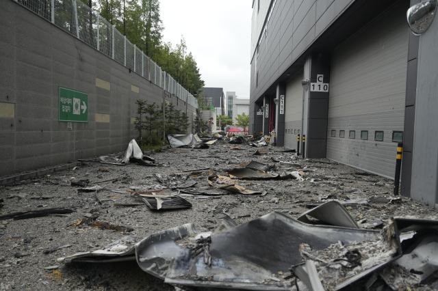 A debris-covered access road between loading bays numbered C110 through C113 with an emergency assembly point sign on the wall to the left at the Coupang Warehouse in Incheon 20260720 AJP Han Jun-gu